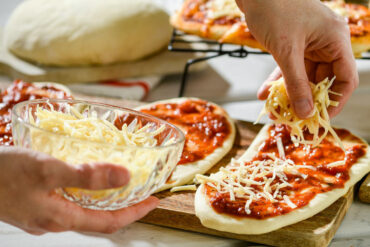 a bowl of shredded cheese with someone using it to make mini pizzas