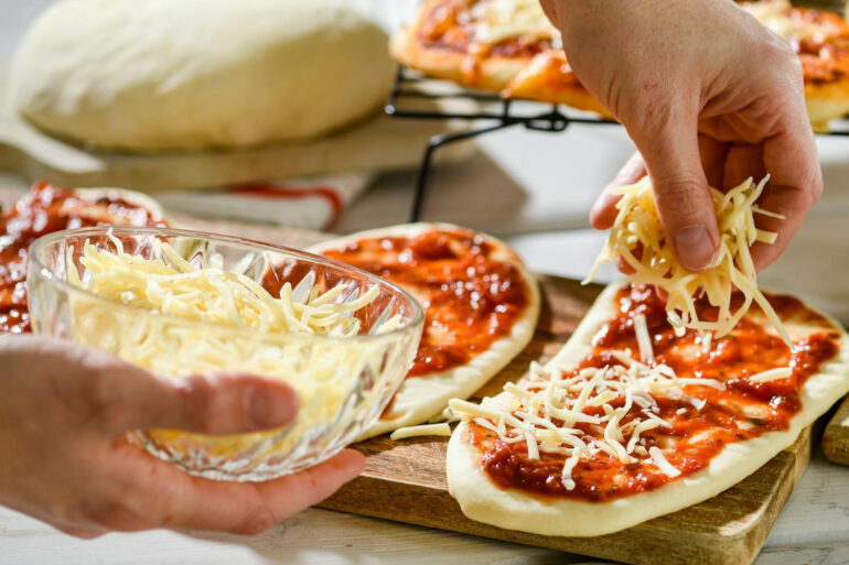 a bowl of shredded cheese with someone using it to make mini pizzas