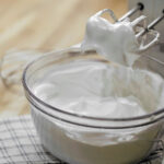 A bowl of whipped cream with mixer on kitchen counter, ready for culinary use