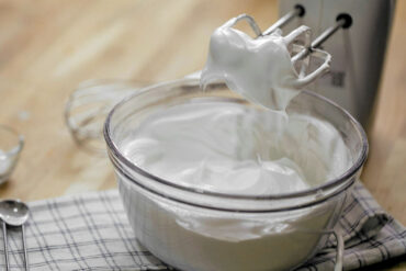 A bowl of whipped cream with a mixer on a kitchen counter, ready for culinary use