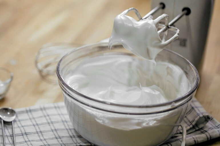 A bowl of whipped cream with a mixer on a kitchen counter, ready for culinary use