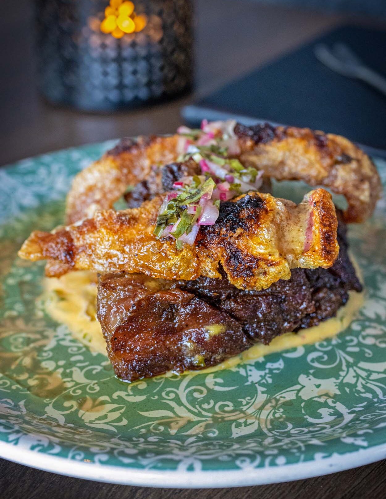 Crisped pork belly with chicharrones at Amada, served on a decorative green patterned plate with pickled radish and herb garnish