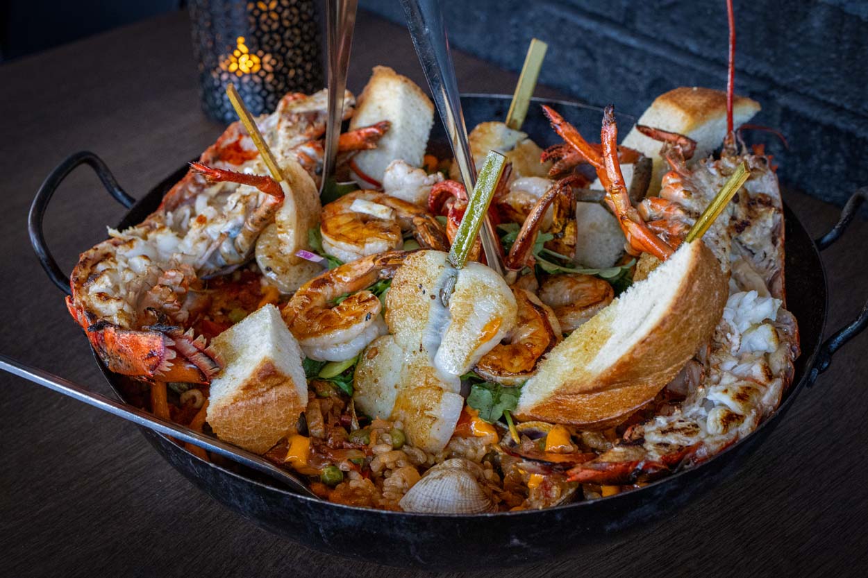 Mariscos paella at Amada served in a large black pan, loaded with lobster, shrimp, scallops, mussels, clams, and squid over saffron rice with crusty bread