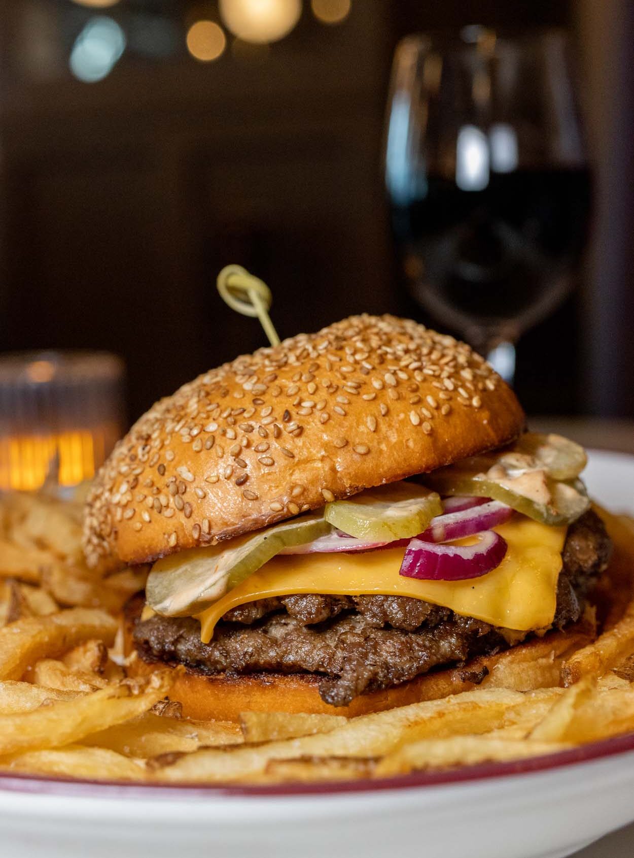 Cheeseburger Royale at Chez Frites, a towering double smash patty burger with melted American cheese, pickles, and red onions on a sesame bun, served with golden hand-cut fries and a glass of red wine