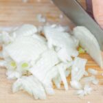 white onions being cut with a knife on a wood cutting board