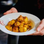 Freshly cooked golden roasted potatoes served on a white plate, held by hands.