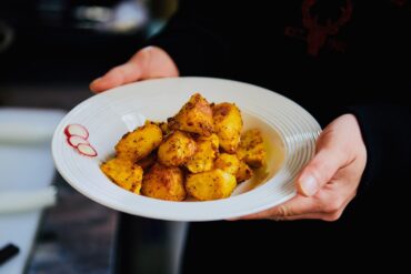 Freshly cooked golden roasted potatoes served on a white plate, held by hands.