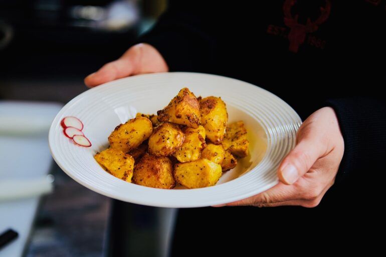 Freshly cooked golden roasted potatoes served on a white plate, held by hands.