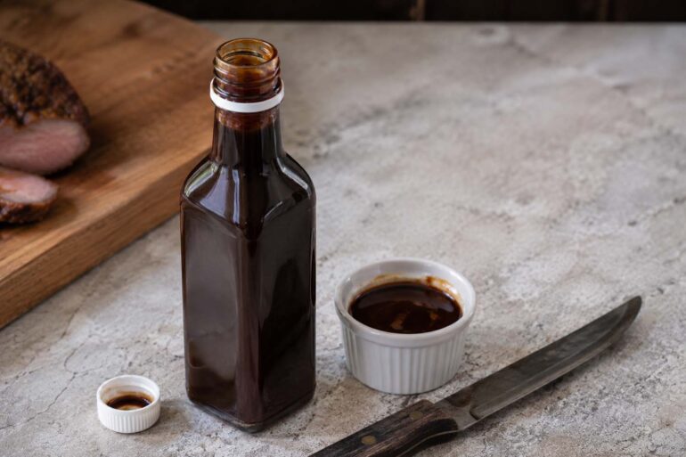 An opened bottle of A1 steak sauce on a kitchen counter next to a steak knife and a small ramekin of sauce