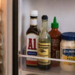 A bottle of A1 steak sauce on a refrigerator shelf next to other condiments, door slightly open