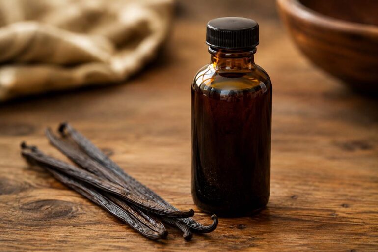 Dark amber glass bottle of pure vanilla extract with vanilla beans beside it on a wooden surface