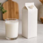 Glass of fresh white milk beside an open milk carton on a clean kitchen counter