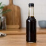 Glass bottle of Worcestershire sauce on a wooden kitchen counter, dark brown sauce visible through bottle