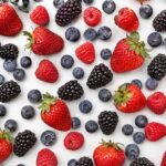 A flat lay of fresh strawberries, blueberries, raspberries, and blackberries on a white background, all unwashed and dry
