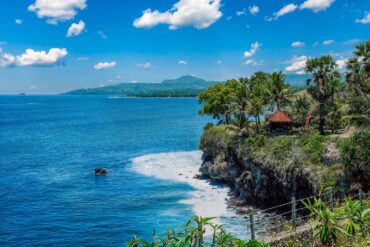 Stunning coastal view of Bali with a cliffside villa and lush palm trees under a clear blue sky