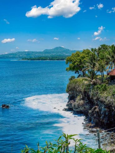Stunning coastal view of Bali with a cliffside villa and lush palm trees under a clear blue sky