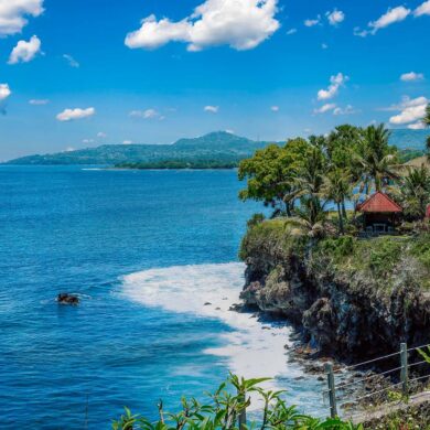 Stunning coastal view of Bali with a cliffside villa and lush palm trees under a clear blue sky