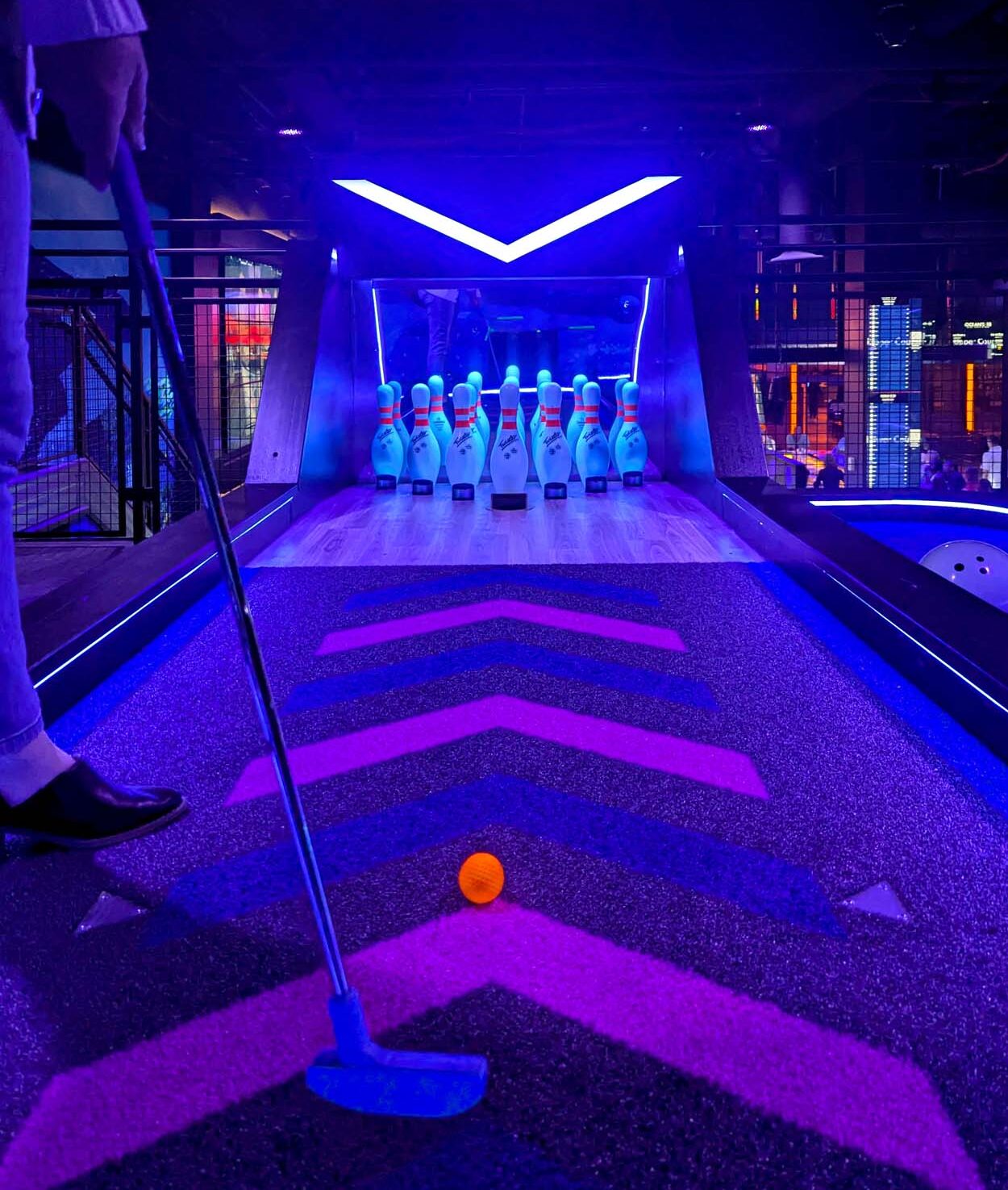 Neon-lit mini golf hole at Ocean's 18 designed like a bowling lane with glowing pins at the end of a chevron-patterned putting surface