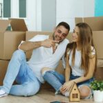 Happy couple sitting on floor in new house. Young man give keys to his girlfriend