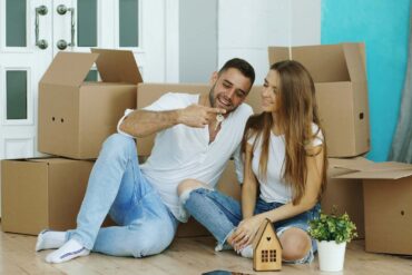 Happy couple sitting on floor in new house. Young man give keys to his girlfriend