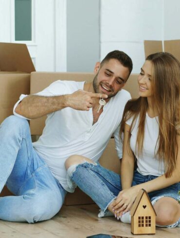 Happy couple sitting on floor in new house. Young man give keys to his girlfriend