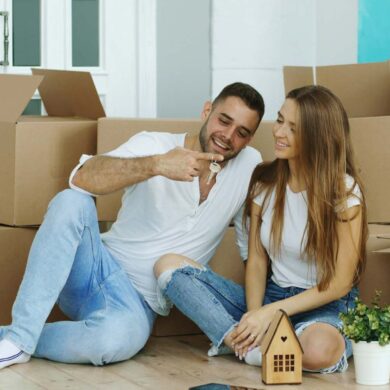 Happy couple sitting on floor in new house. Young man give keys to his girlfriend