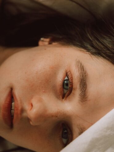 Captivating portrait of a young woman with bold eyebrows on a bed, enveloped in soft light