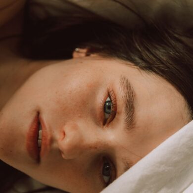 Captivating portrait of a young woman with bold eyebrows on a bed, enveloped in soft light