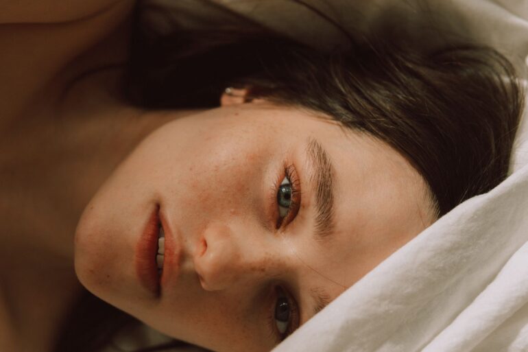 Captivating portrait of a young woman with bold eyebrows on a bed, enveloped in soft light