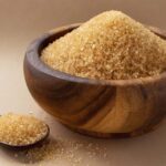 Close-up of raw brown sugar in a rustic wooden bowl with a spoon