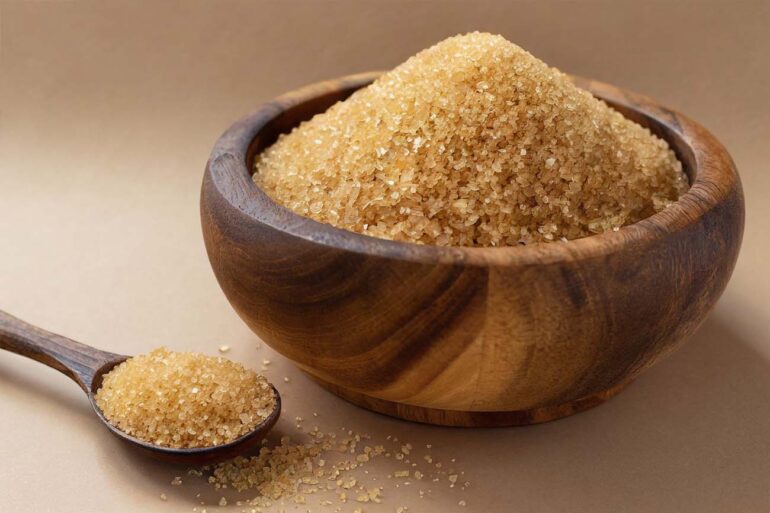 Close-up of raw brown sugar in a rustic wooden bowl with a spoon
