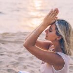 A woman meditates peacefully on a serene beach during sunset