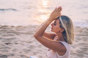 A woman meditates peacefully on a serene beach during sunset