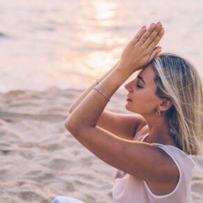 A woman meditates peacefully on a serene beach during sunset