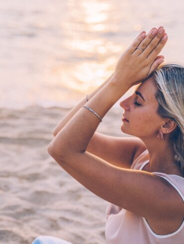 A woman meditates peacefully on a serene beach during sunset