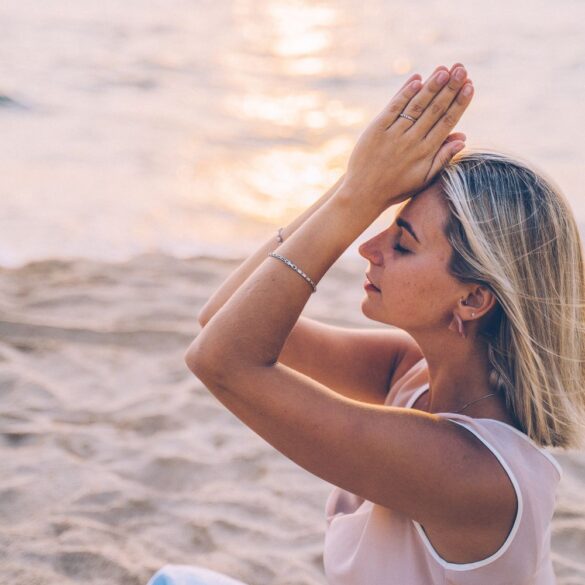 A woman meditates peacefully on a serene beach during sunset