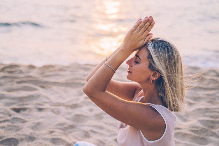 A woman meditates peacefully on a serene beach during sunset
