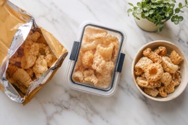 an open bag of commercial pork rinds next to an airtight storage container, alongside a small bowl of fresh chicharrones