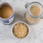 an open canister of plain dry breadcrumbs next to a sealed glass airtight jar of breadcrumbs, with a small bowl of fresh homemade breadcrumbs alongside.
