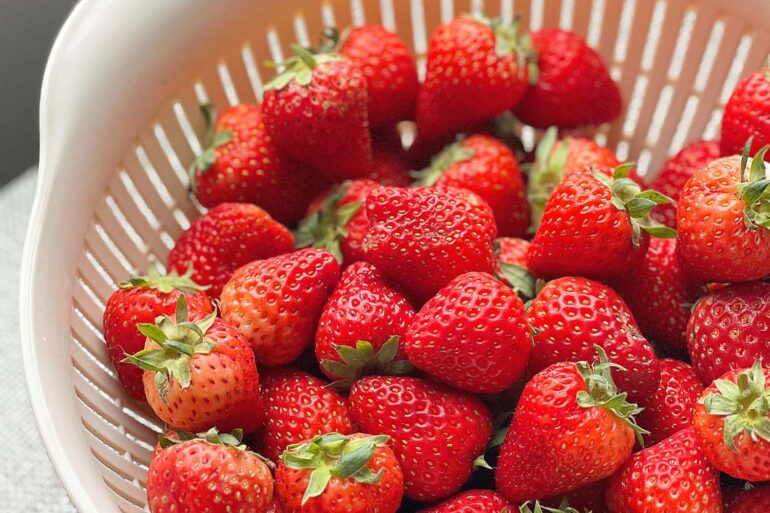 A vibrant collection of fresh strawberries in a white colander,