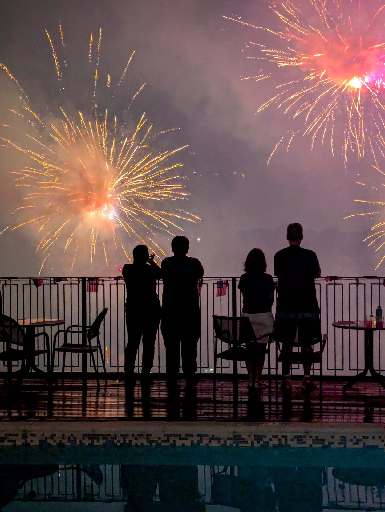 Spectacular multicolor July 4th fireworks display over Lake Kittamaqundi viewed from the rooftop at Merriweather Lakehouse Hotel in Columbia Maryland with guests silhouetted at the pool railing