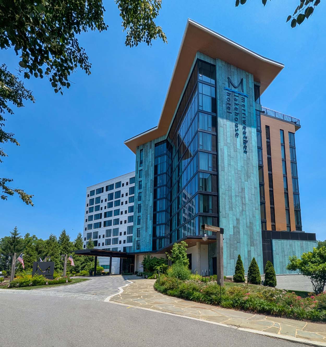 Merriweather Lakehouse Hotel in Columbia Maryland in summer with the glass and copper facade surrounded by lush green trees on a bright July day