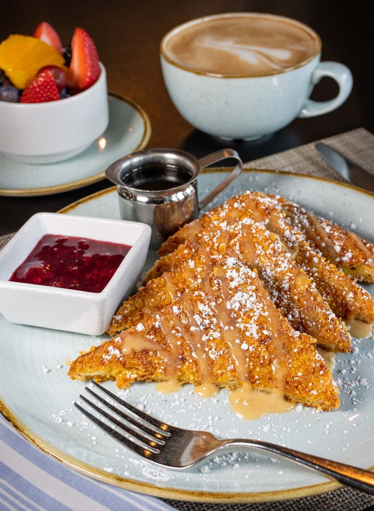 Cornflake crusted French toast at lak restaurant at Merriweather Lakehouse Hotel served with berry compote powdered sugar a pitcher of maple syrup and a latte with latte art