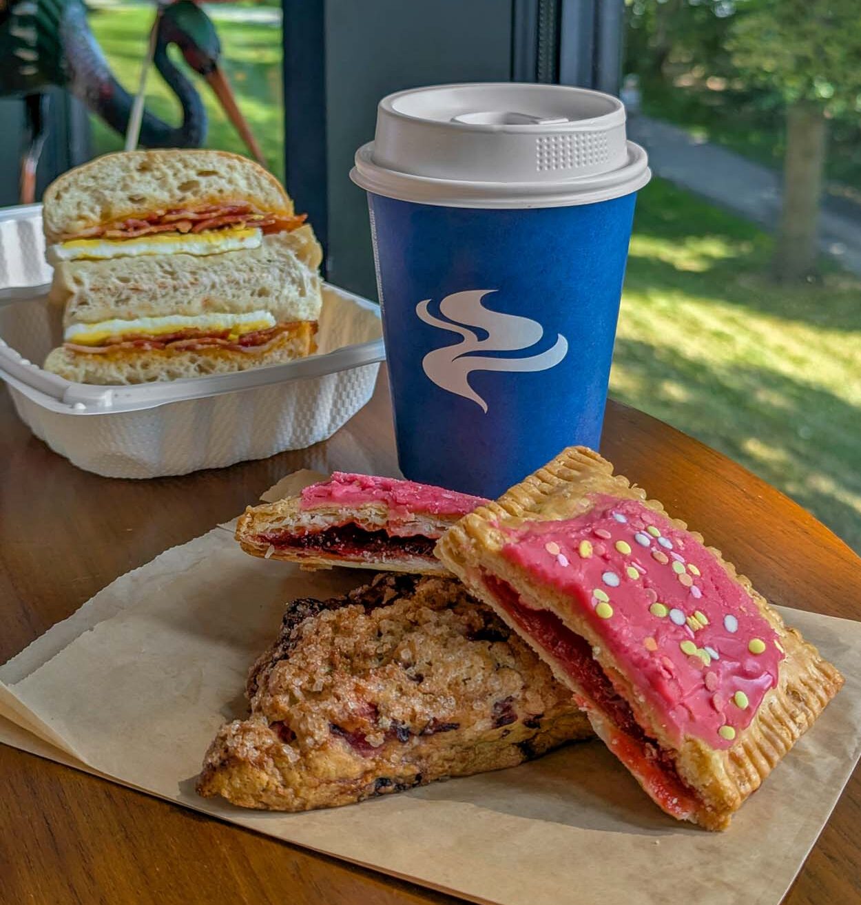Morning pastries at Osprey Cafe at Merriweather Lakehouse Hotel including a berry scone homemade pop tart with pink icing a breakfast sandwich on focaccia and a Lavazza coffee to go