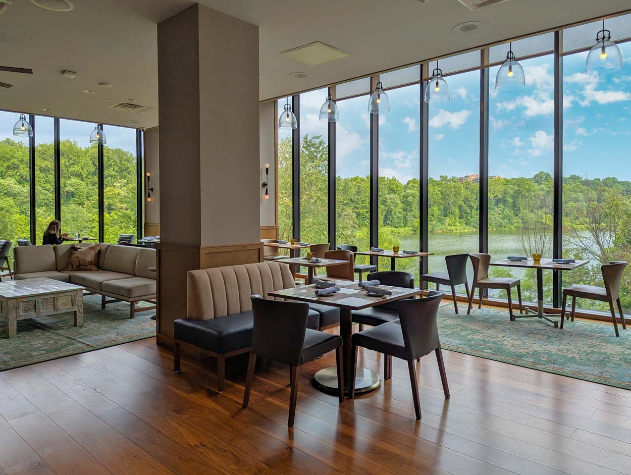 The Rookery Bar and Lounge at Merriweather Lakehouse Hotel in Columbia Maryland with the horseshoe bar teal tile green barstools and floor to ceiling windows overlooking the lake and summer trees