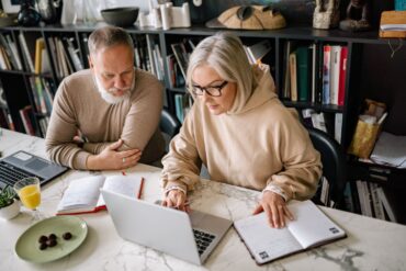 An older couple collaborating about retirement plans on laptops in a home office setting.