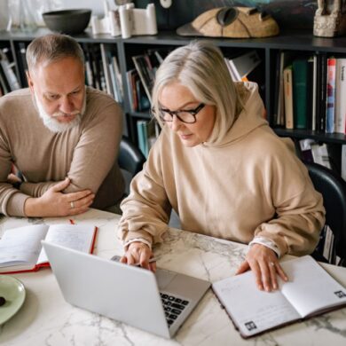 An older couple collaborating about retirement plans on laptops in a home office setting.
