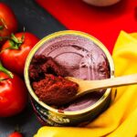 A colorful flat lay of fresh vined tomatoes and a can of tomato paste with a wooden spoon