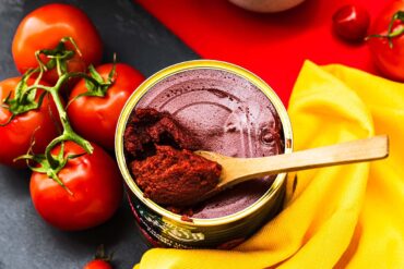 A colorful flat lay of fresh vined tomatoes and a can of tomato paste with a wooden spoon