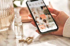 Hand holding phone scrolling wellness content next to peptide supplement vials, illustrating the peptides trend